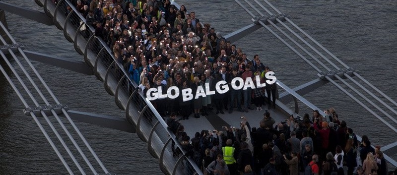 A group of people stand on a bridge holding large letters spelling 'Global Goals'.