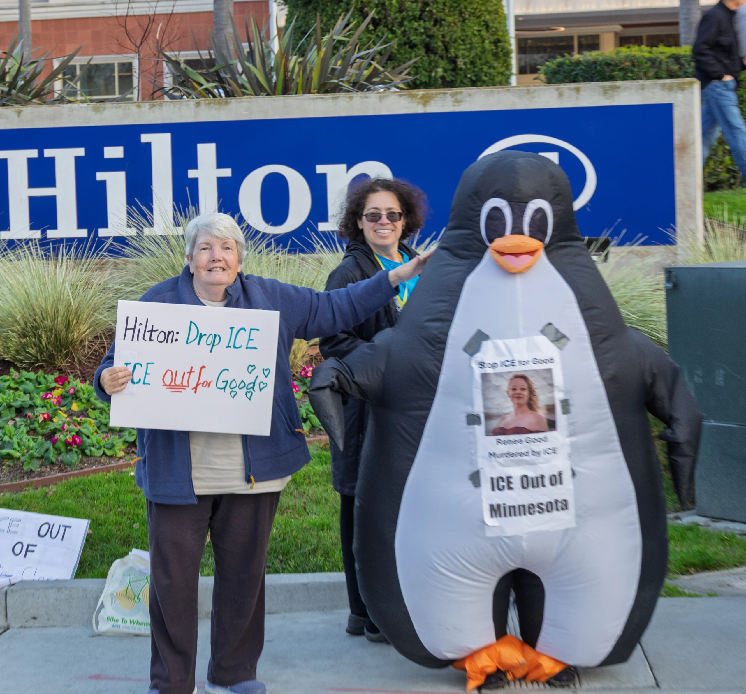 Photograph of protesters outside a Hilton hotel. One protester wears an inflatable penguin costume, another holds a placard reading 'Hilton Drop Ice: Out for Good'