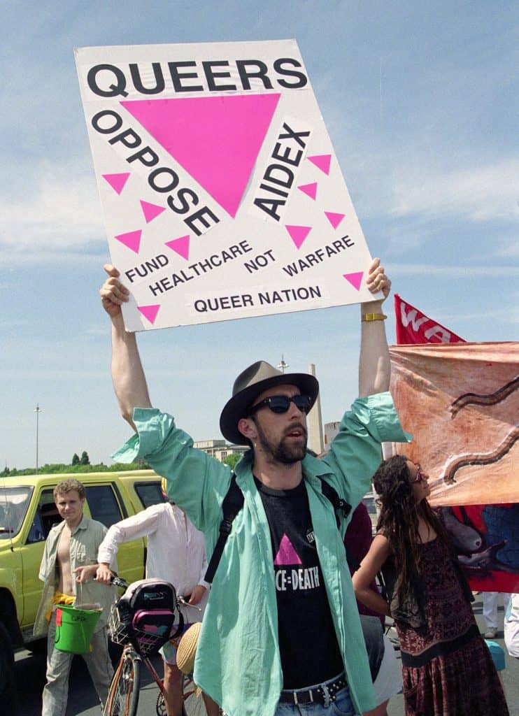 a protestor holding up a sign that says Queers oppose Aidex. Fund Healthcare not Warefare. Queer Nation