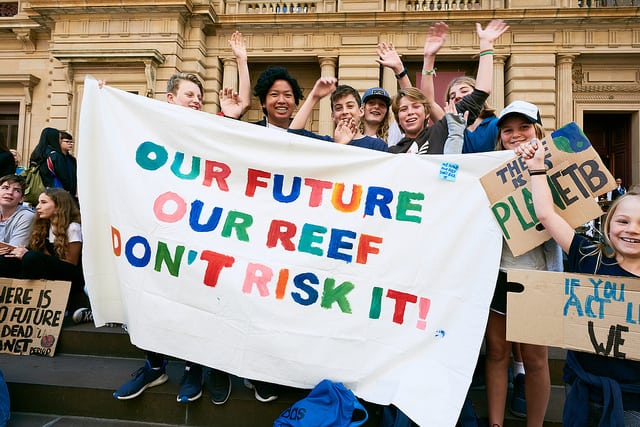 Photograph of students holding a banner reading 'Our Future, Our Reef, Don't Risk It'.