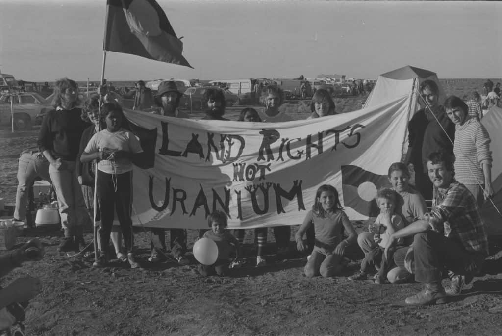Protesters against Honeymoon Uranium mine, NSW, 1982. Protestors include Aboriginal Australians holding sign that says Land Rights not Uranium and holding an Aboriginal flag.
