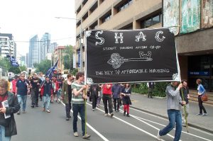 Protestors walking down street holding big banner with words - Student Housing Action Co-operative SHAC - The key to affordable housing