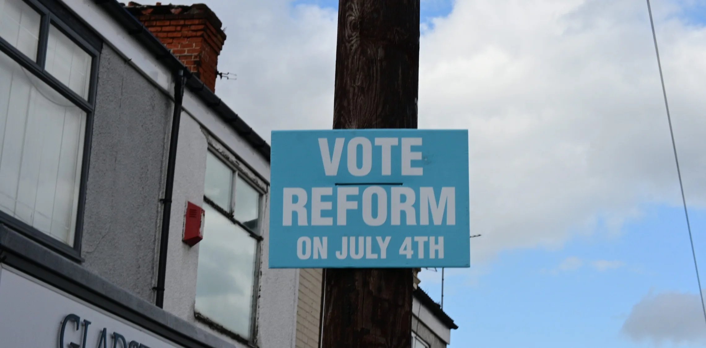 Poster on wooden telegraph pole in front of buildings. Poster reads 'Vote Reform on July 4th'.
