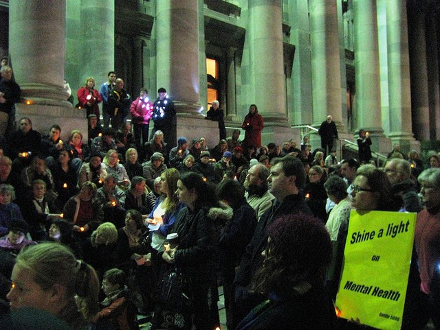 A crowd gathered in the evening, in the foreground a sign reads 'Shine a light on mental health'
