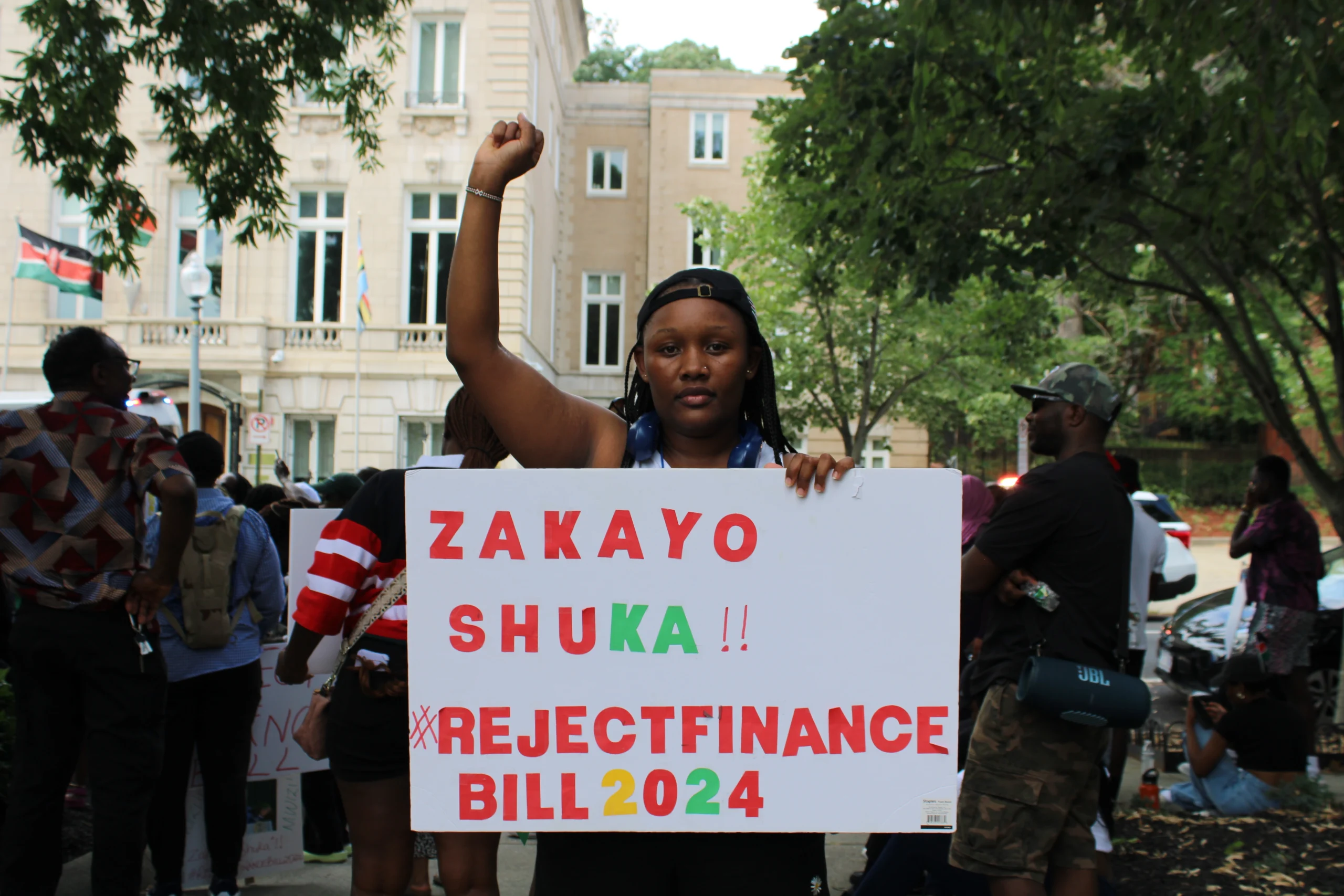 A woman holding a fist in the air and a sign at a protest. The sign reads 'Zakeyo Shuka!! #RejectFinanceBill2024"