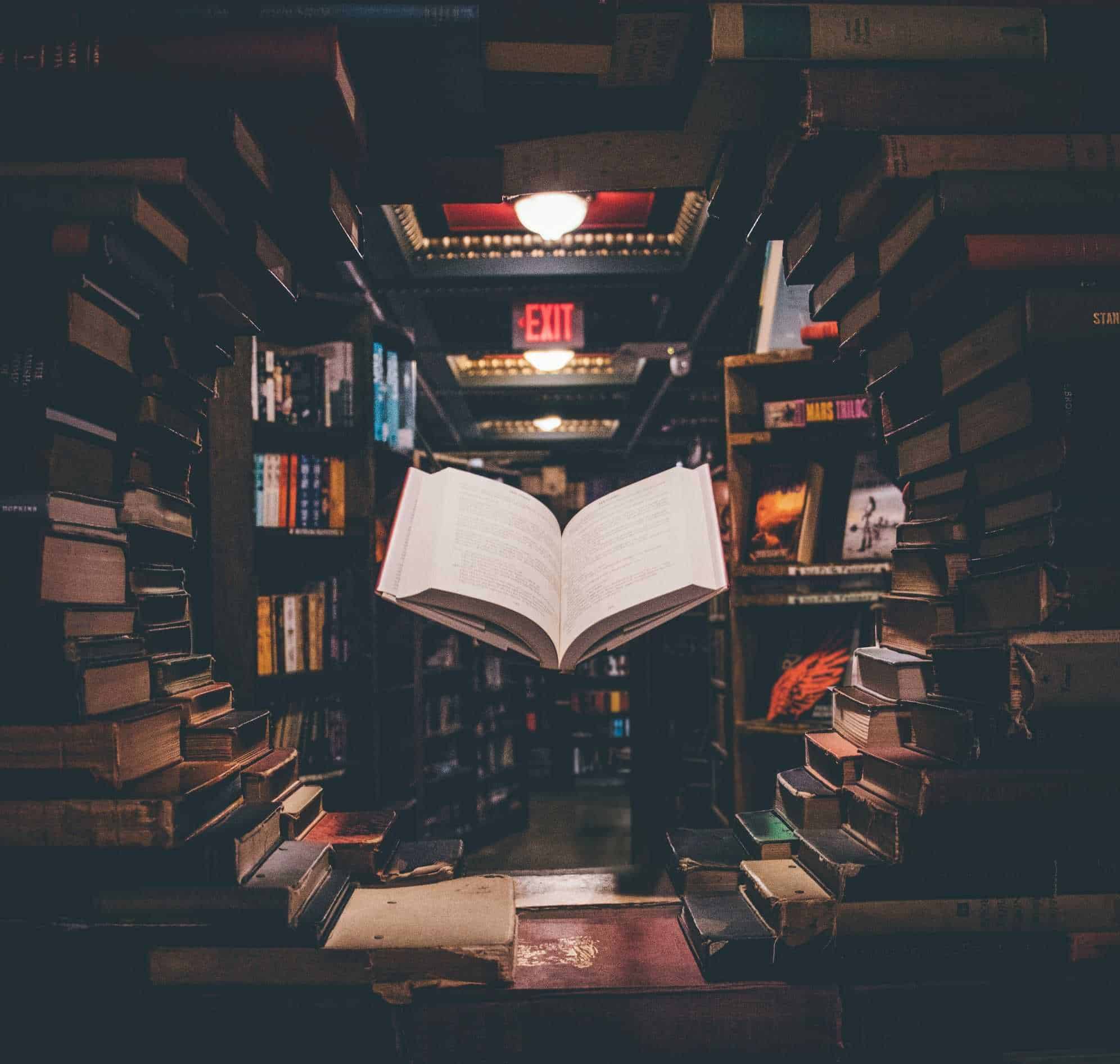 A large pile of books has a circular space cleared with a floating open book in the middle.