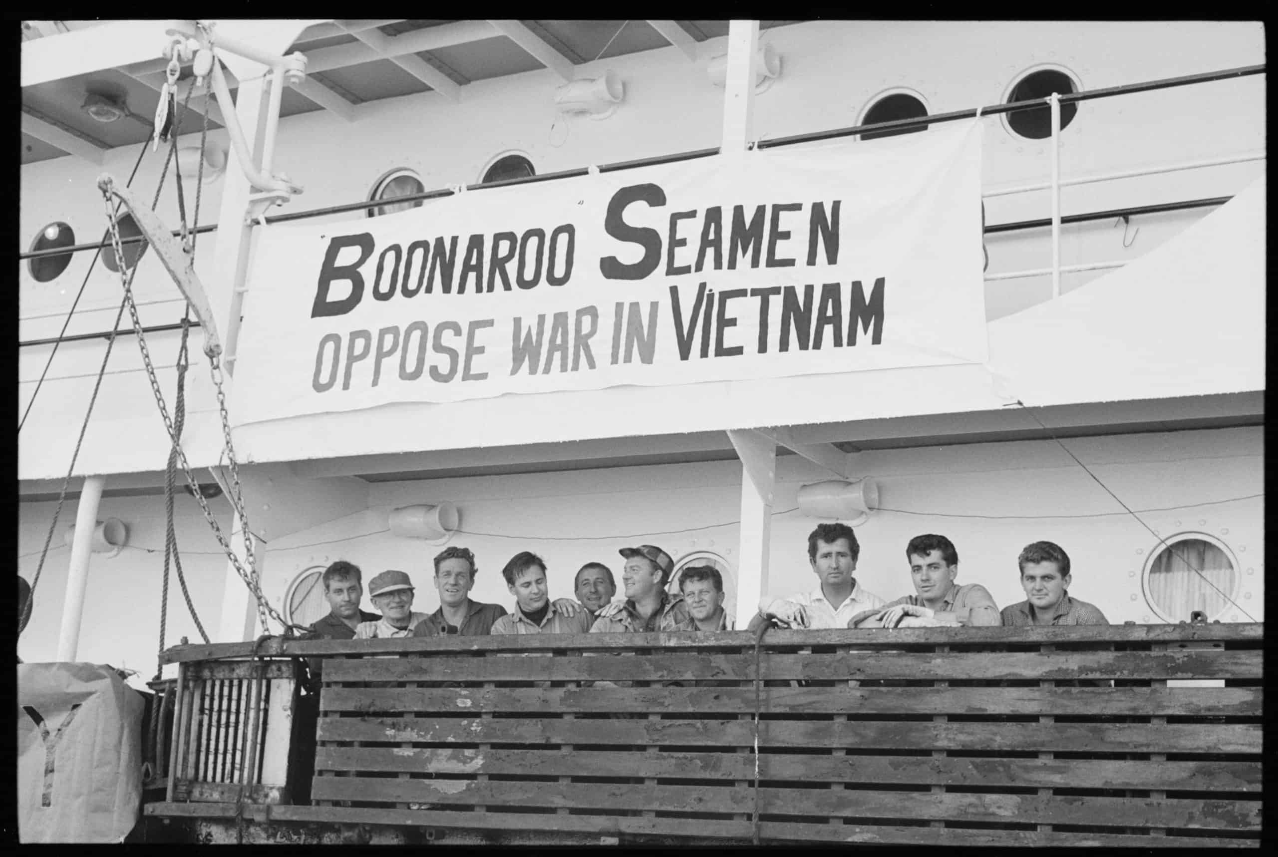A group of men standing at ship's railing with banner above their heads that reads Boonaroo Seamen Oppose War in Vietnam
