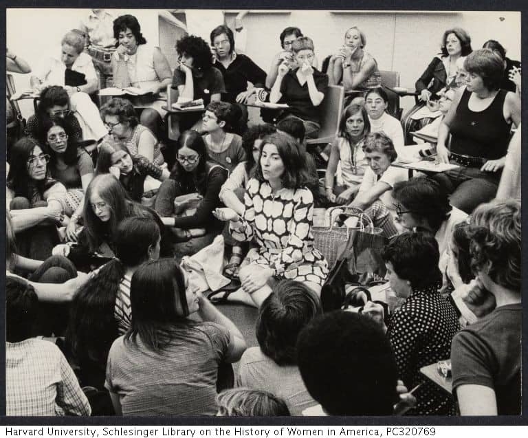 A large group of women sit in a room talking animatedly.