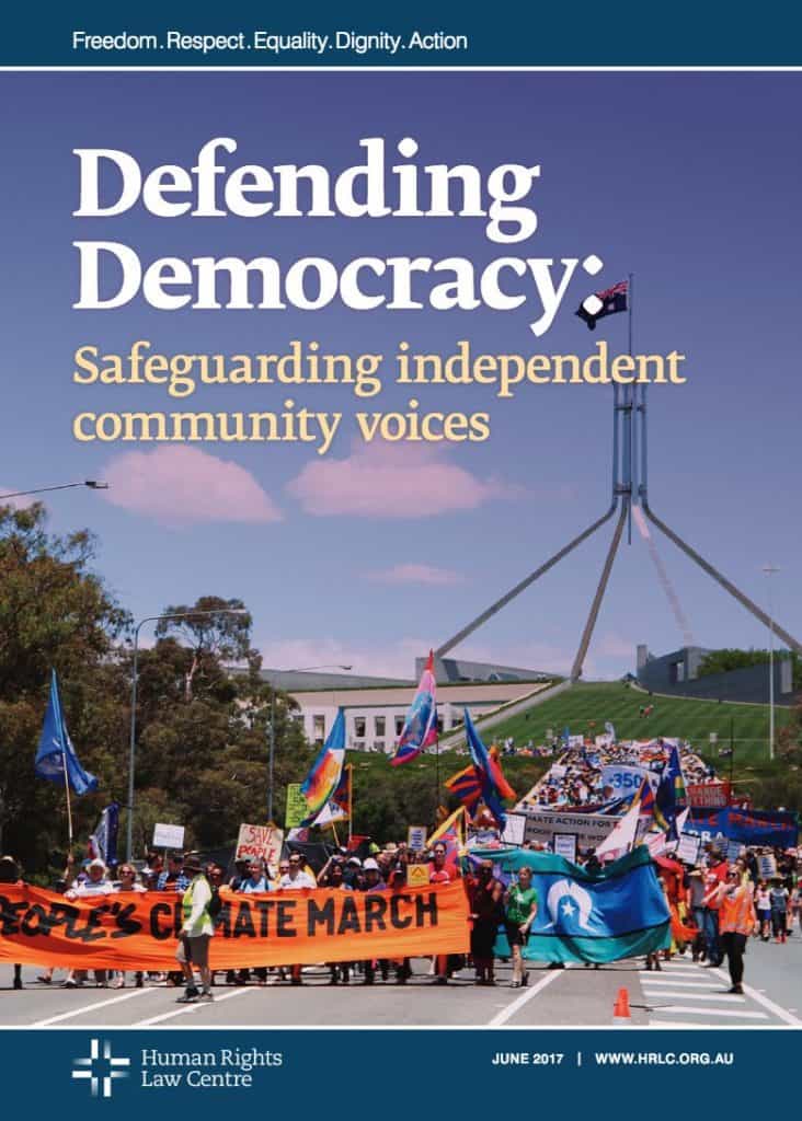 Cover of the Defending Democracy: Safeguarding independent community voices Report. Photograph of a people marching with climate and Indigenous rights banners and flags with Parliament House in the background.