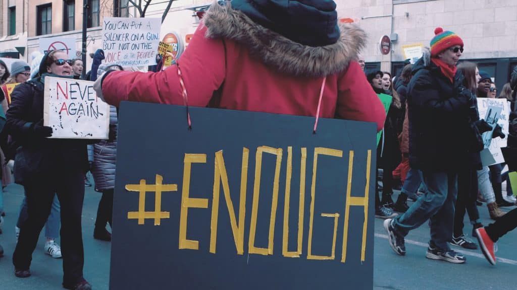 woman in protest carrying a sign saying #enough