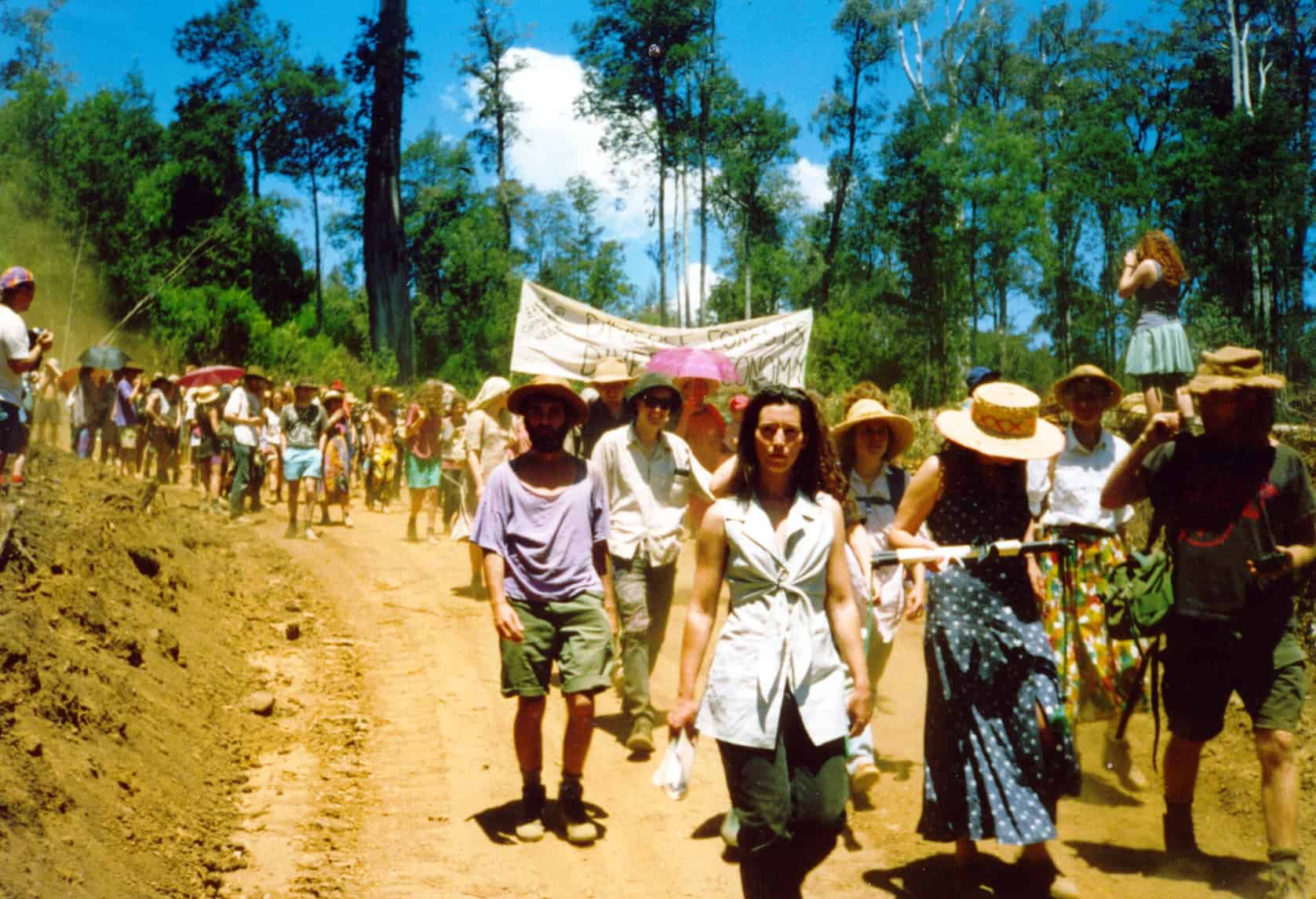 A group of protestors walking down a dirt road. One group is holding a banner that says Diverse Forests.