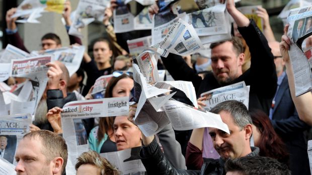 A crowd of people holding up newspapers with squares cut out for them to look through.