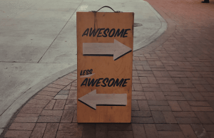 Photograph of a sandwich board on pavement, it reads 'Awesome' with an arrow pointing to the right, and 'Less Awesome' with an arrow pointing to the left.