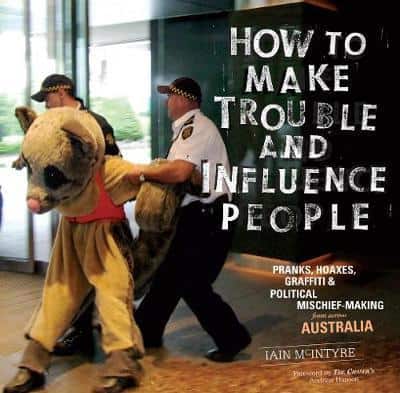 Cover of How to Make Trouble and Influence People. Features a photograph of someone in a sugar glider outfit being removed from an area by two policeman.
