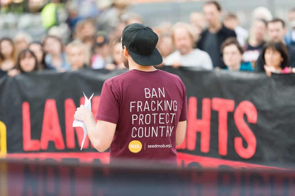Man addressing anti-fracking rally in the Northern Territory, Australia wearing a tshirt that says 'Ban fracking Protect Country' with the logo SEED