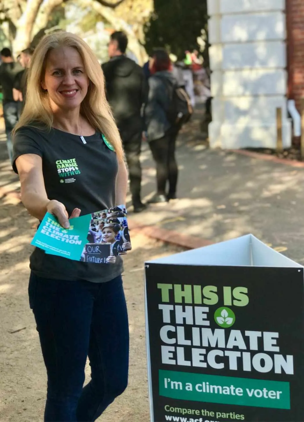 Kathryn McCallum hands out climate policy scorecards at a polling booth in Macnamara electorate in Melbourne during the 2019 Australian federal election. There is a cardboard stand that reads 'This is the Climate Election'.|audio player