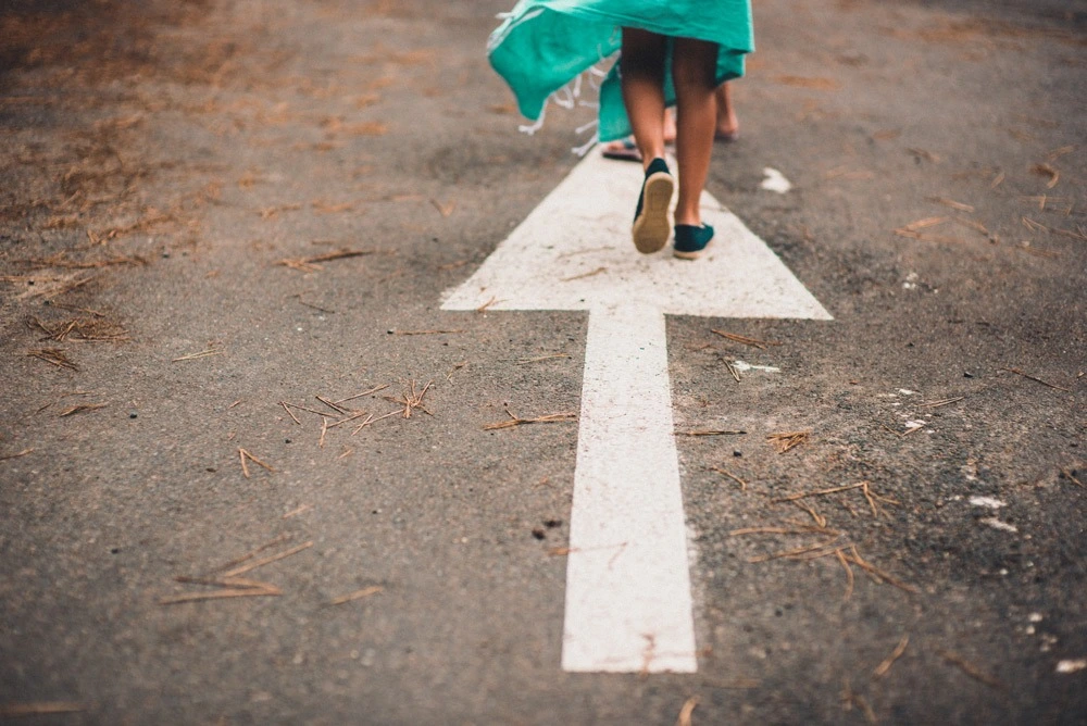 Young person walking on a white arrow on the road.