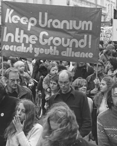 A group of protestors with large banner that reads Keep Uranium in the ground