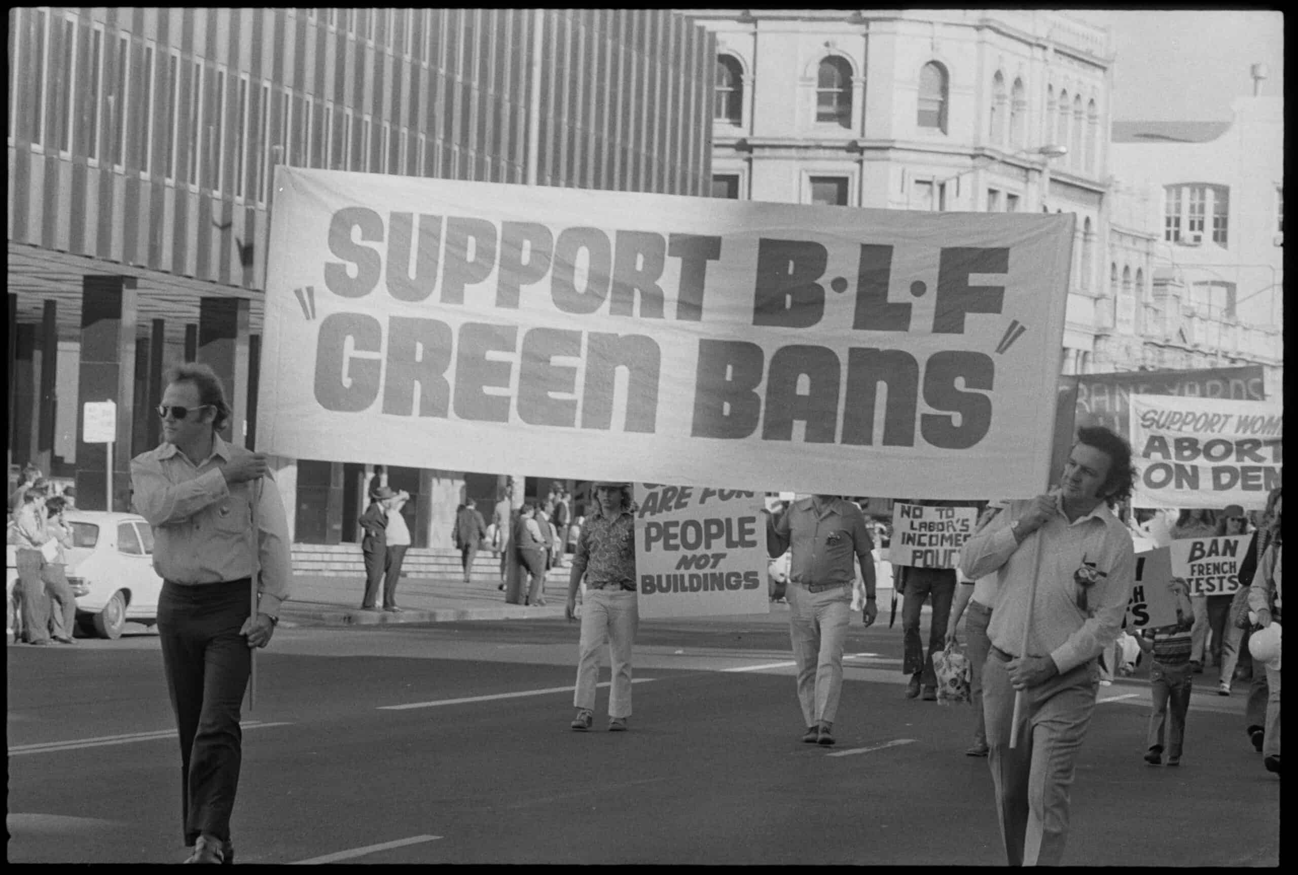Two May Day marchers carrying a banner in 1973 that reads "Support BLF Green Bans"||||May Day marcher holding a sign reading Builders Labourers support Peoples Plan for the Rocks.|Poster with a red No cross and the words This House with one sixth of Glebe will be destroyed to make way for the already outmoded