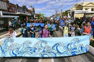 Happy people march down High St in Northcote Victoria. They hold banners painted with waves.