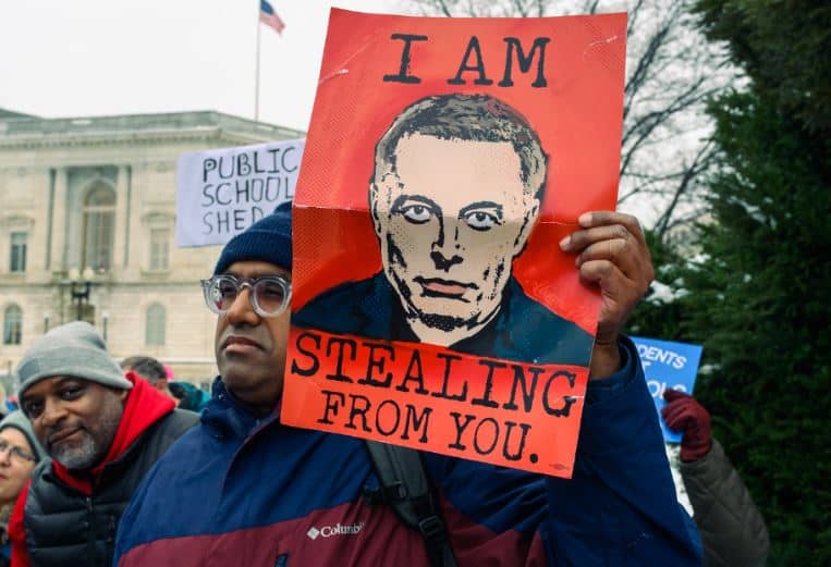 A man at a protest holding a sign with a picture of Elon Musk and the words "I am stealing from you."|Tweet parodying Elon Musk that says Dear Elon