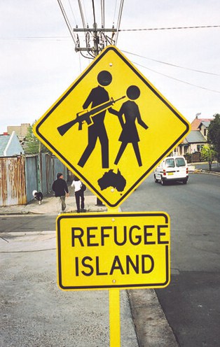 A photograph of a street sign. It has been modified so 'Refuge Island' reads as 'Refugee Island'. The sign includes two figures, one is now holding a gun and a small map of Australia has been added to the picture.