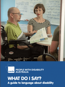 Male wheelchair user sitting at table reading a report with a woman looking on