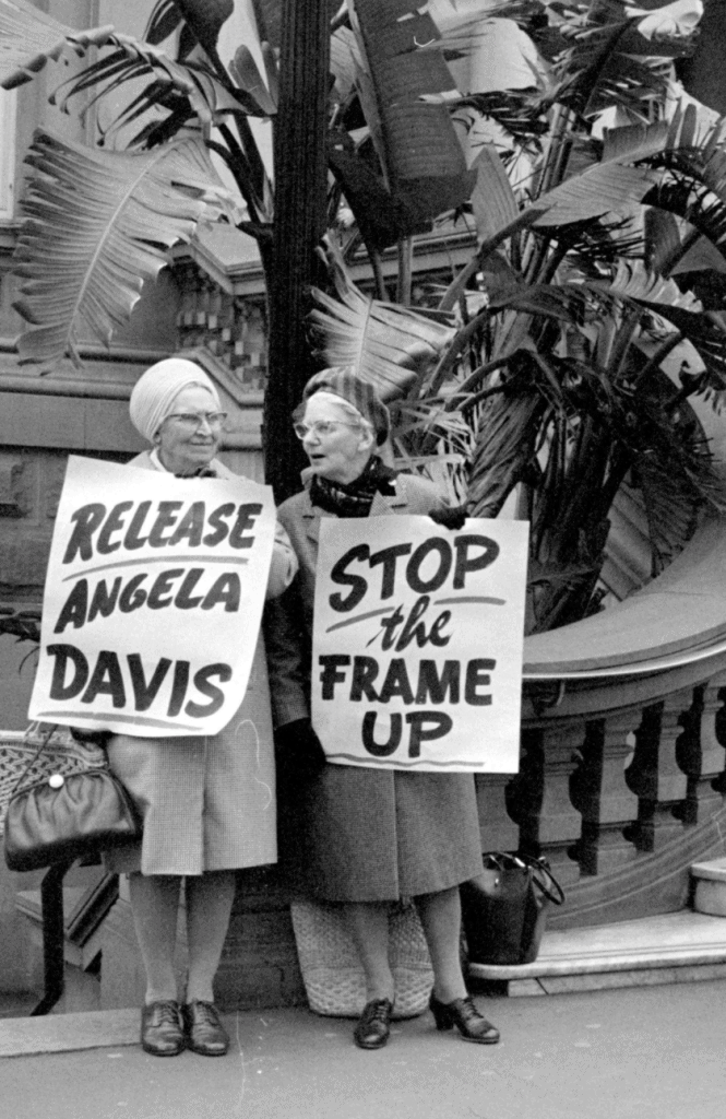 Two older ladies holding posters that say "Release Angela Davis" and "Stop the frame up"