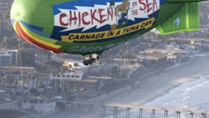 blimp flying over city. On the blimp it says Chicken of the Sea, Carnage in a Tuna Can, Greenpeace.