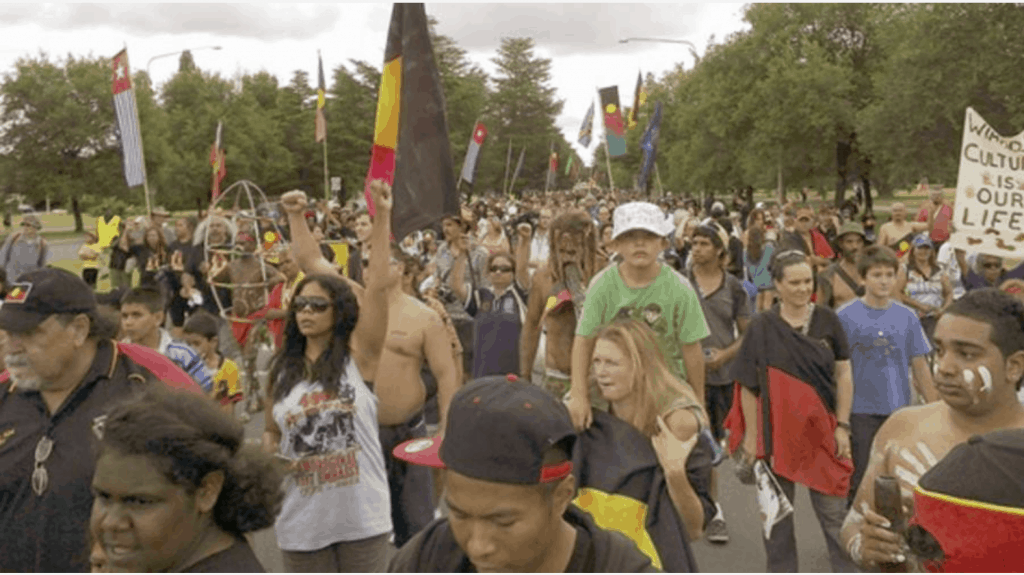 Protestors marching on Survival Day holding banners and Australian Aboriginal flags