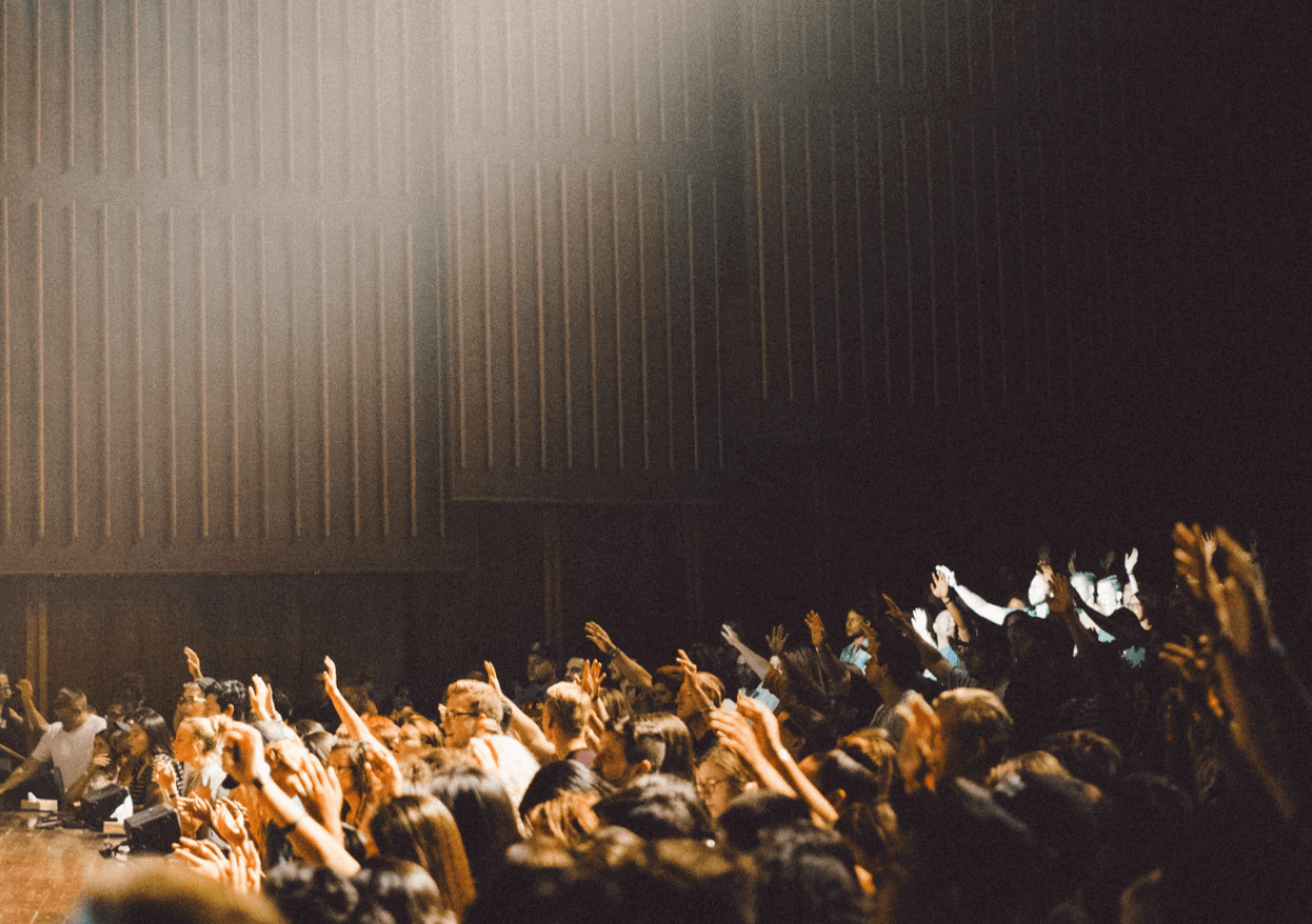 A large crowd gathered in a conference room with hands raised.