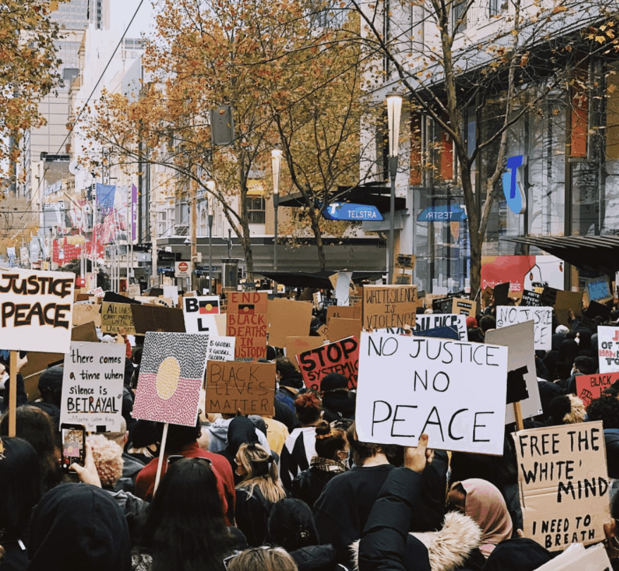 A crowded street with protestors with signs that say No Justice, No Peace and Free the white mind