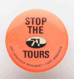 Circular orange badge featuring at centre the slogan 'Stop the 71 tours' in black text and 'Anti-apartheid movement - fight apartheid' at bottom of badge.