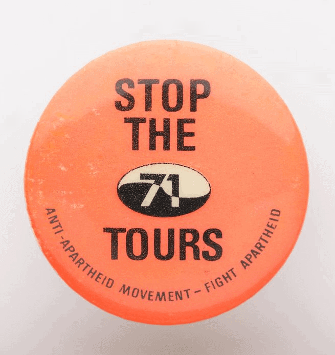 Circular orange badge featuring at centre the slogan 'Stop the 71 tours' in black text and 'Anti-apartheid movement - fight apartheid' at bottom of badge.