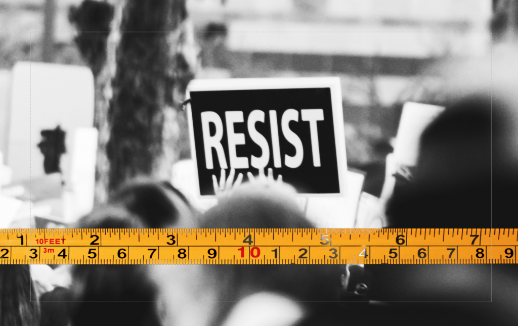yellow tape measure on top of a black and white photo of protestors in a crowd and one banner being held up says Resist