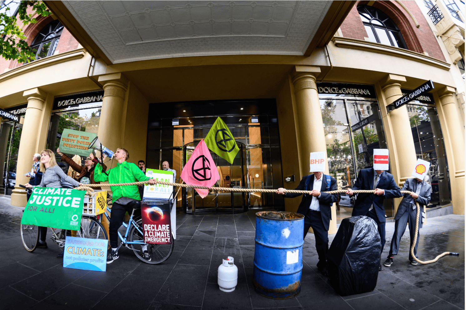 Climate activists engage in tug of war stunt. At one end of the rope are a group of climate activists. At the other end of the rope are people in suits with fossil fuel company logos covering their faces.