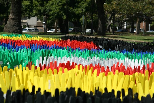 Photograph of part of the Sea of Hands - plastic hands are 'planted' in lines of bright colour (black, yellow, red, white, green, blue).