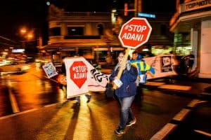 Protestors walk across the street with Stop Adani banners and placards.