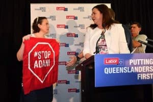 Protestor holding Stop Adani sign on stage with Queensland Premier Annastacia Palaszczuk.