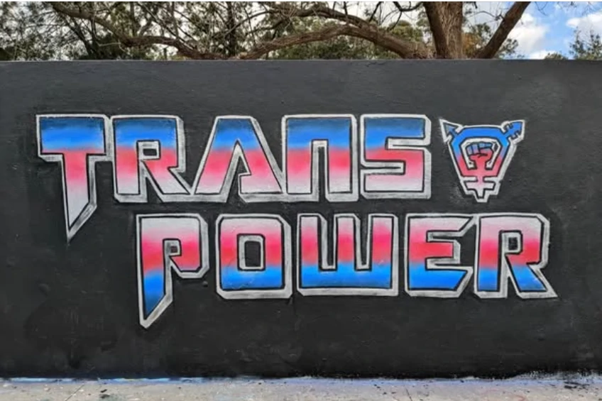Mural that reads Trans Power in Transformer style lettering||Someone wearing a tshirt with a picture of Tony Abbott with FKD text - in the style of KFC Kentucky Fried Chicken.|Photograph of the front of a house with a sign in the window: 'Escaped refugees welcome here'.|A photograph of a helicopter suspended beneath a larger helicopter with the text:'Bronwyn Bishop Getting Road Side Assistance'|Sticker: 'Don't Buy Apartheid'.|Cover of a 1934 edition of Proletariat magazine featuring an impressive block cut. giant red hand holding a policeman|Poster: 'To Arms! Capitalists