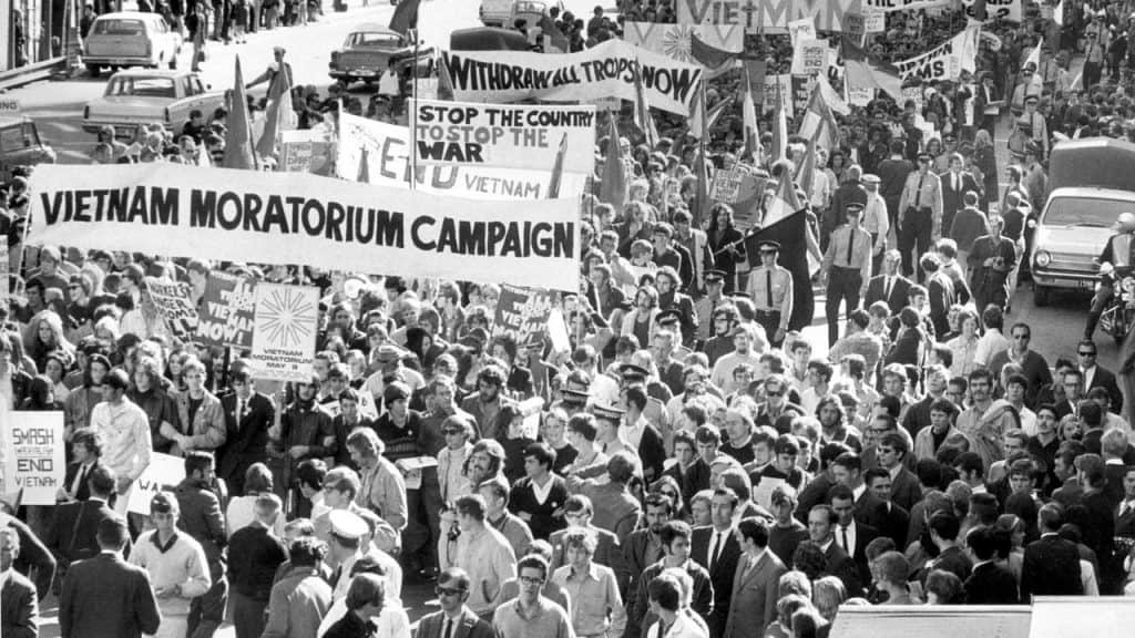 Black and white photograph of a large crowd of protestors. Banners include 'Vietnam Moratorium Campaign' and 'Stop the Country to Stop the War'.