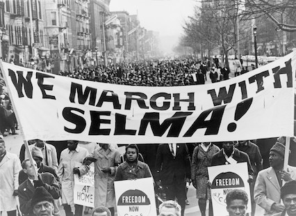 A large crowd marching behind a banner saying: We march with Selma!
