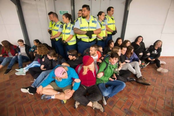 A group of police officers stand side by side, surrounded by seated activists with arms interlinked.