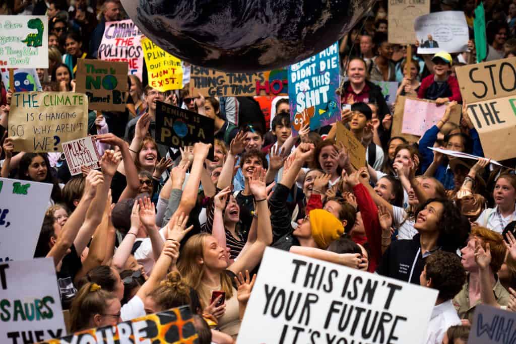 A large group of young protestors all reaching their hands up bouncing a giant inflatable earth. Some are holding banners. One reads This isn't your future. The crowd look happy.