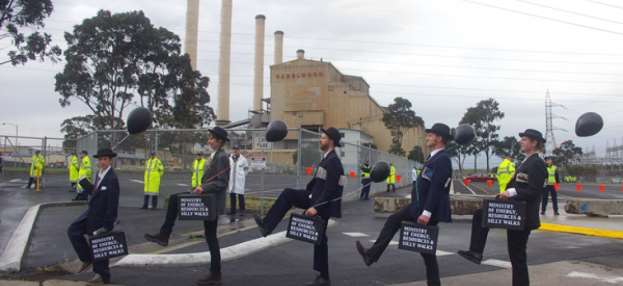 Photograph of people dressed in suits and bowler hats and brief cases walking together in front of a coal fired power station.