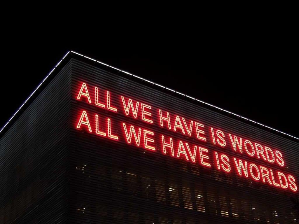 Photo of neon sign reading 'ALL WE HAVE ARE WORDS; ALL WE HAVE ARE WORLDS'