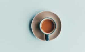 A teal espresso cup filled with brown coffee, on a slightly lighter teal table, taken from above.