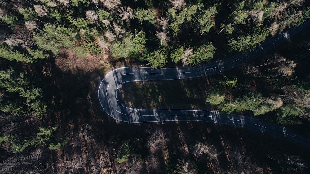 Arial view of a road through a forrest. The road curls back on itself, changing directly completely.