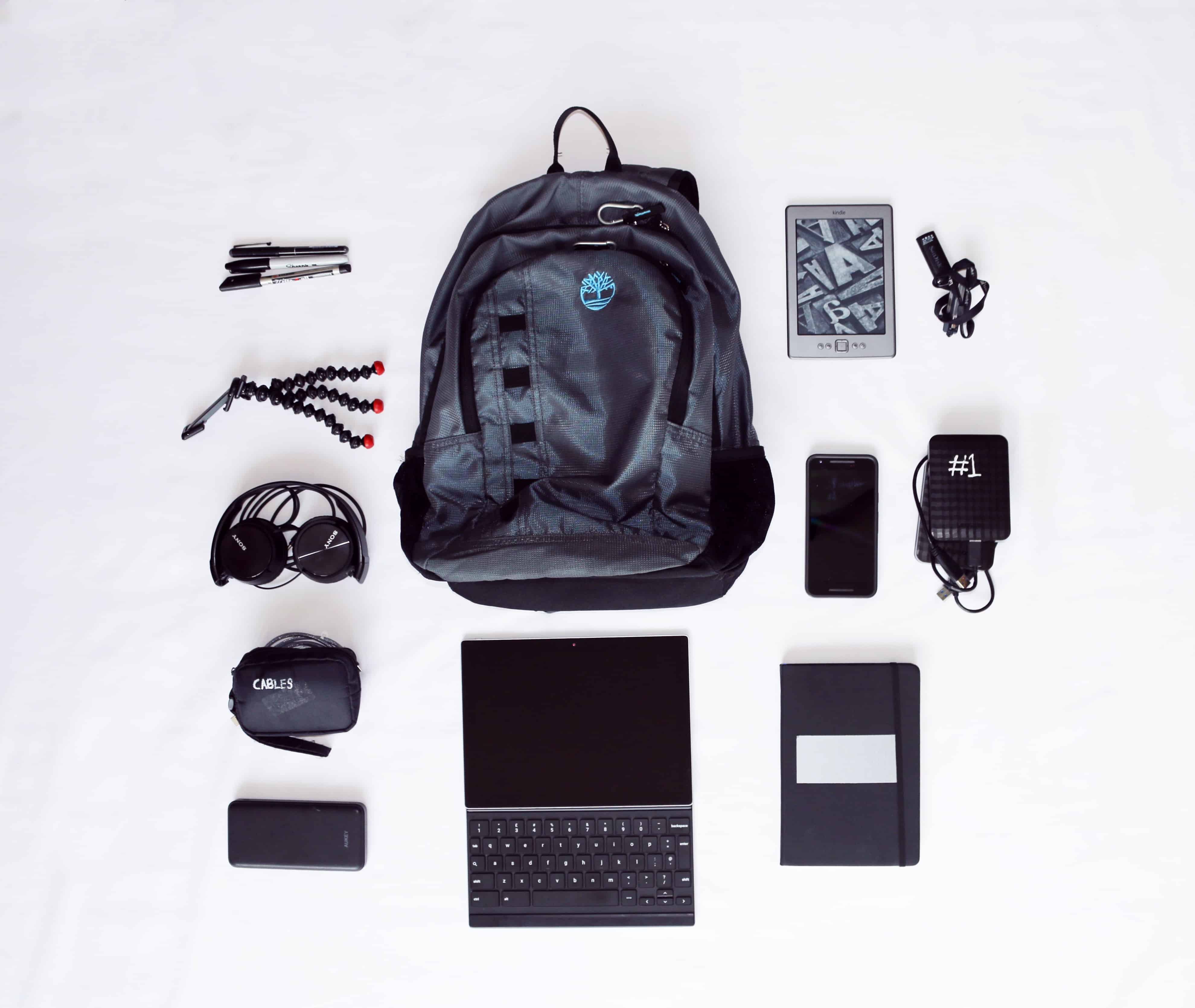 backpack with contents laid around the outside of backpack such as headphones, laptop, cords, etc.