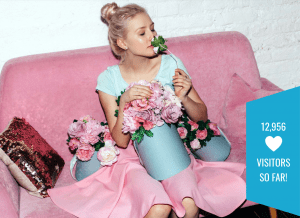 Screenshot of the Ecomark website. A model in blue sits on a bright pink couch, with flowers on her lap. She is smelling one of them. Overlaid on the image is the text '12956 visitors so far!'